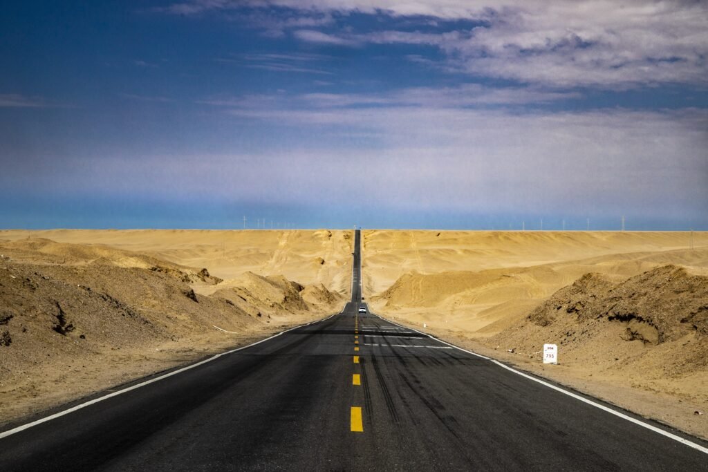 Long straight asphalt road stretching into the distant horizon through an open desert landscape under a clear blue sky, symbolizing forward direction and decisive action.