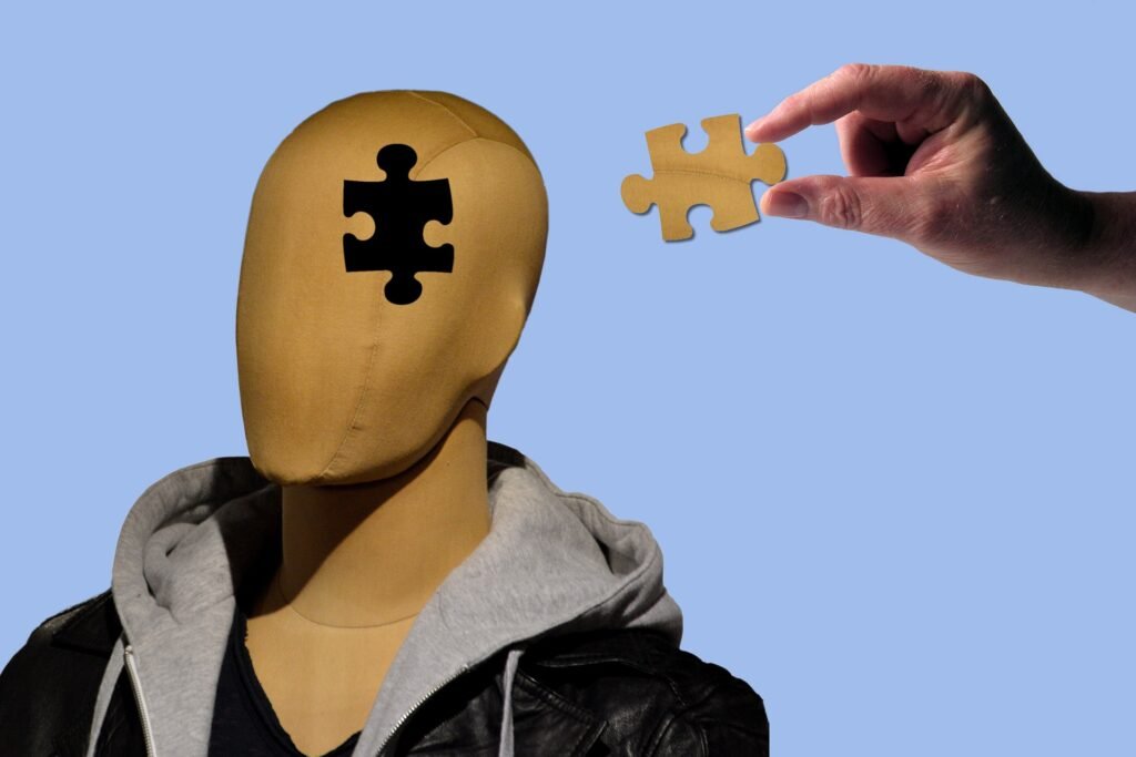 Mannequin head with missing puzzle piece in forehead, with a hand holding the matching piece nearby against a clear blue background, symbolizing the integration of thoughts and mindset.
